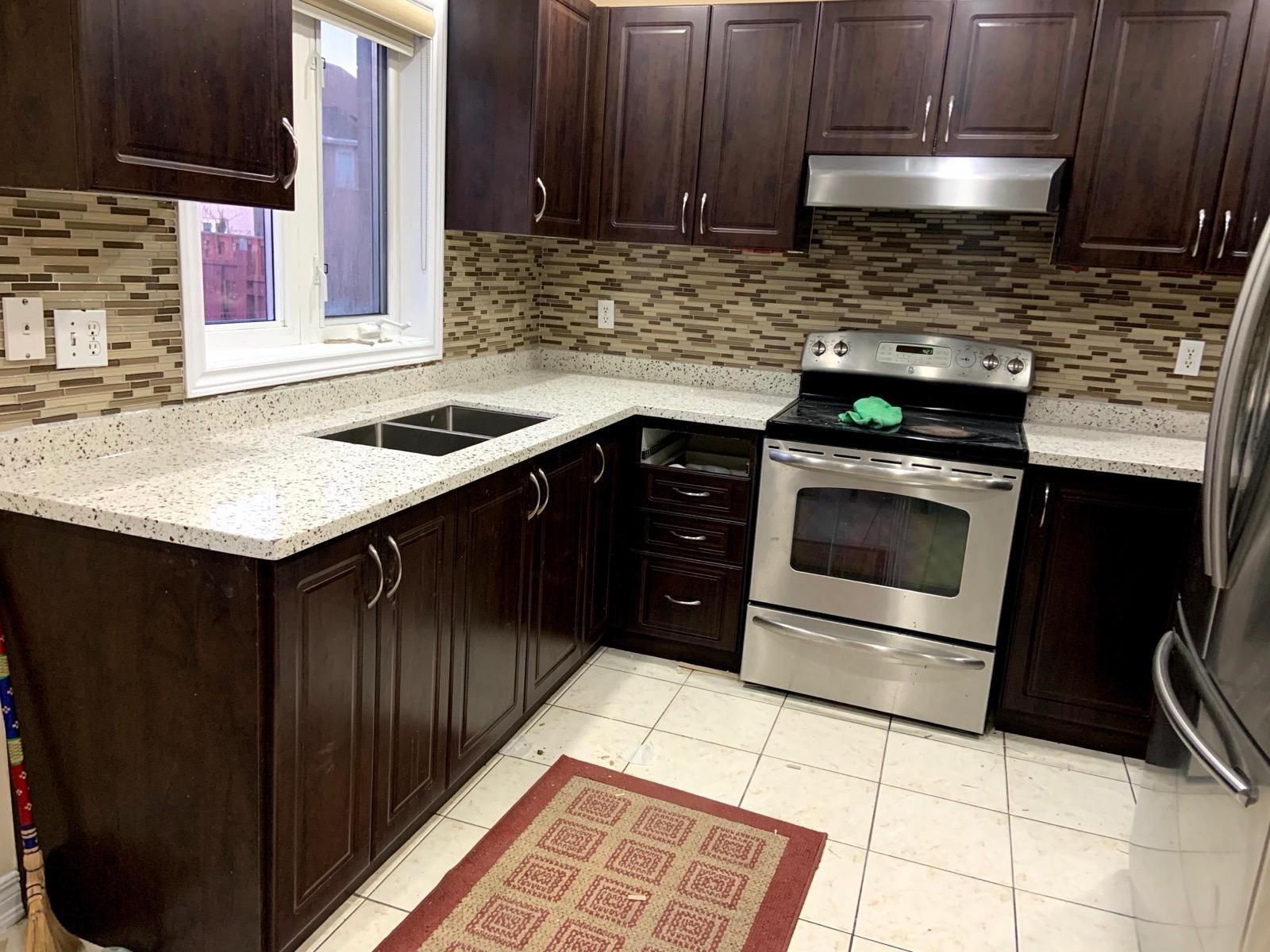 L-shaped kitchen with white speckled countertops and dark wood cabinets